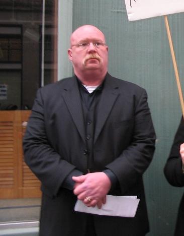 Anti Wilford Brimley standing in front of a wall at the 10th Feb IRL [[PROJECT CHANOLOGY|Project Chanology